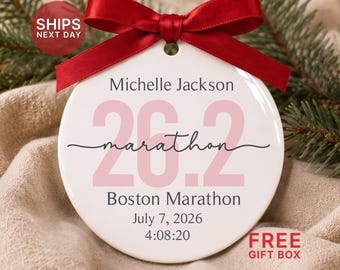 May include: A round white ceramic ornament featuring a red satin ribbon bow at the top. The text reads Michelle Jackson, 26.2, marathon, Boston Marathon, July 7, 2026, and 4:08:20 in black and light pink lettering.