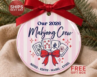 May include: A round ceramic ornament with a pink and white striped background, topped with a red satin ribbon. It features the text Our 2026 Mahjong Crew, illustrations of four mahjong tiles, a red bow, and the names Agnes, Edith, Mabel, Ethel.
