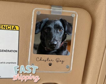 May include: A clear acrylic car visor photo holder with a picture of a black dog. The dog's name, "Chester Bay", is written in cursive below the photo, along with a paw print. The visor is tan.