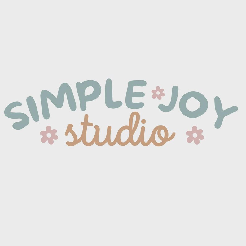 Peut inclure: Logo "SIMPLE * JOY" en bleu sarcelle et "studio" en beige, avec de petites fleurs roses, sur fond blanc. Le design a un aspect artisanal et fantaisiste.