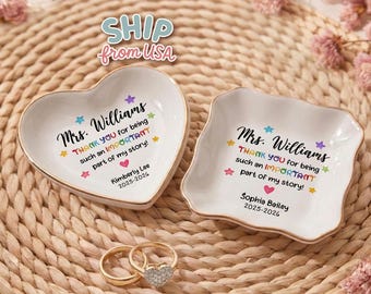 May include: Two white ceramic ring dishes, one heart-shaped and one square, with gold trim. Each dish has a personalized message with the name "Mrs. Williams" and the text "THANK YOU for being such an IMPORTANT part of my story!" Two gold rings with a heart-shaped diamond are also present.