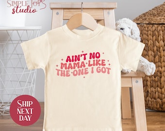 May include: A cream-colored baby t-shirt with a pink and red graphic that says "Ain't no mama like the one I got".