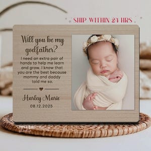 May include: A wooden picture frame with the text "Will you be my godfather?" and a photo of a baby. The frame includes the baby's name, Harley Marie, and the date 08.12.2025. The frame is light brown and has a natural wood grain.