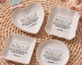 May include: Four white ceramic trinket dishes in heart, square, and round shapes, each with a gold rim. The dishes feature floral designs and the text "OCCUPATIONAL THERAPIST" with a name below. The phrase "NEVER FORGET THE DIFFERENCE THAT YOU MAKE" is also printed.