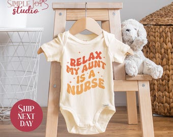 May include: A cream-colored baby onesie with short sleeves and a graphic that reads "Relax My Aunt Is A Nurse" in a retro font with orange, red, and yellow colors.
