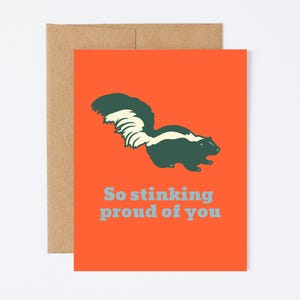 May include: Orange card with a black and white skunk illustration and the text "So stinking proud of you" in blue.