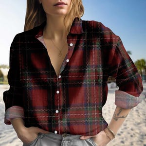 Op de afbeelding: Een button-down shirt met een rood en zwart geruit patroon. Het shirt heeft lange mouwen en een kraag. De stof heeft een licht getextureerde uitstraling. Het shirt is aan de bovenkant opengeknoopt en onthult een glimp van de borst van de drager en een gouden ketting.