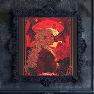 Puede incluir: Impresión artística enmarcada que presenta el perfil de una mujer con largo cabello rubio, sobre un paisaje rojo y naranja con alas de dragón. La obra de arte está en un marco negro ornamentado, con el nombre "Rhaenyra" en la parte inferior.