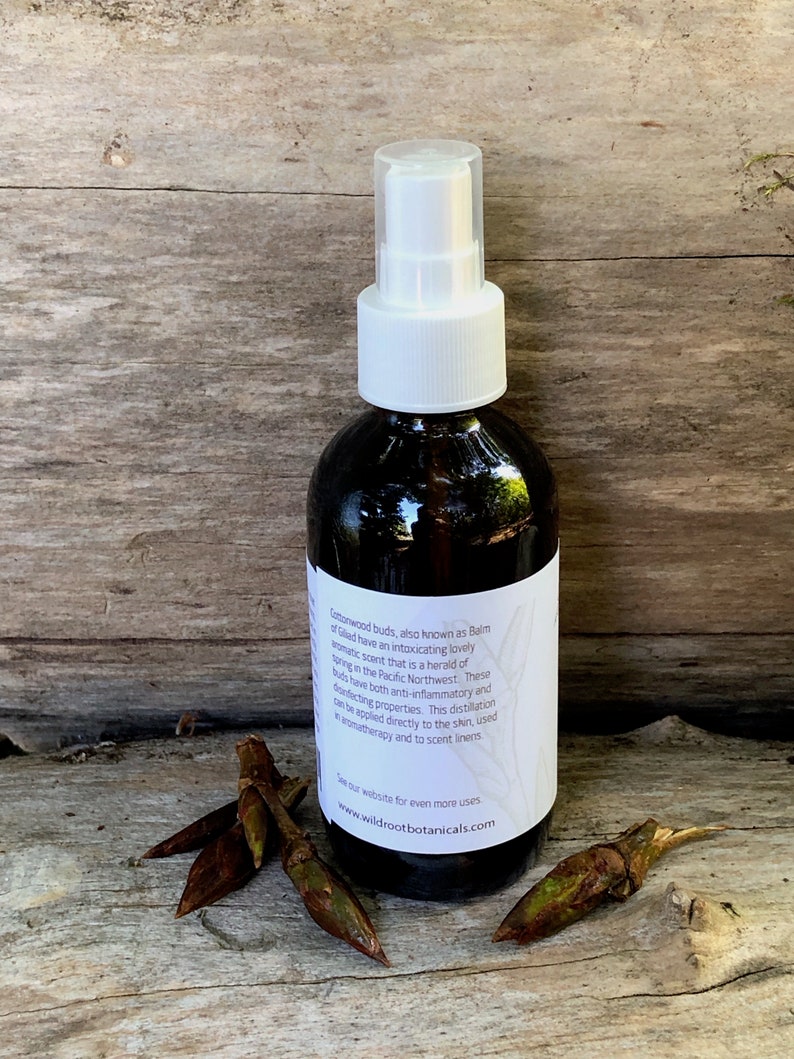 May include: A brown glass bottle with a white spray top filled with a clear liquid. The bottle has a white label with text that reads "Cedarwood buds, also known as Balm of Gilead have an intoxicating lovely aromatic scent that is a herald of spring in the Pacific Northwest. These buds have both anti-inflammatory and disinfecting properties. This distillation can be applied directly to the skin, used in aromatherapy and to scent linens. See our website for even more uses www.wildrootbotanicals.com"