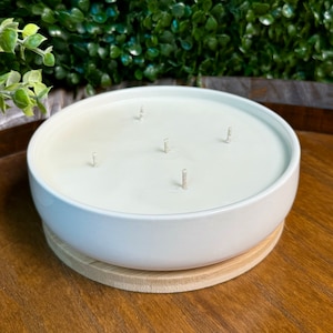 May include: White ceramic candle bowl with four wicks and a wooden base. The candle is unlit.