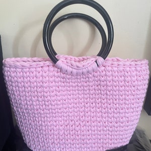 Peut inclure: Un sac cabas en crochet rose avec des anses doubles en boucle noire. Le sac est fait d'un fil épais et texturé et a un design simple et classique.