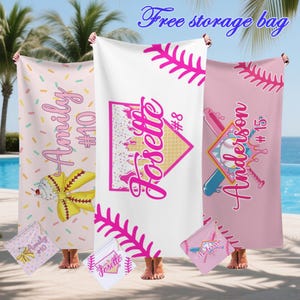 May include: Three personalized baseball-themed beach towels in pink and white. Each towel features a name and number, with baseball-related graphics. The towels are displayed outdoors near a beach, with a free storage bag.