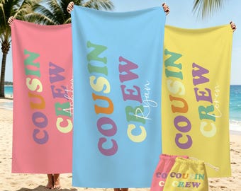 May include: Three rectangular beach towels in pink, light blue, and yellow, each featuring the text COUSIN CREW in colorful, retro-style lettering. Two small drawstring bags in pink and yellow with the same text are positioned at the bottom.