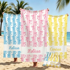 May include: Three rectangular beach towels featuring vertical stripes and a repeating bow pattern. The left towel is blue and white with the name Lelissa, the center is pink and white with Lelissa, and the right is yellow and white with Carissa.