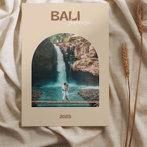 Op de afbeelding: Een beige reisdagboek met het woord "BALI" in bruine letters bovenaan en het woord "Indonesia" in een scriptlettertype. Het dagboek bevat een foto van een waterval en een stel. Het jaar "2025" staat onderaan gedrukt.