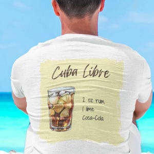 Puede incluir: Camiseta blanca con una receta de cóctel Cuba Libre. El diseño incluye las palabras "Cuba Libre", una ilustración del cóctel y los ingredientes: 2 oz de ron, 1 lima y Coca-Cola.