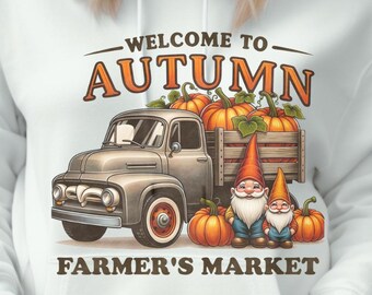 May include: White hoodie with a graphic featuring a vintage truck loaded with pumpkins, the text "WELCOME TO AUTUMN FARMER'S MARKET", and two gnome figures. The model is wearing a mustard yellow beanie.