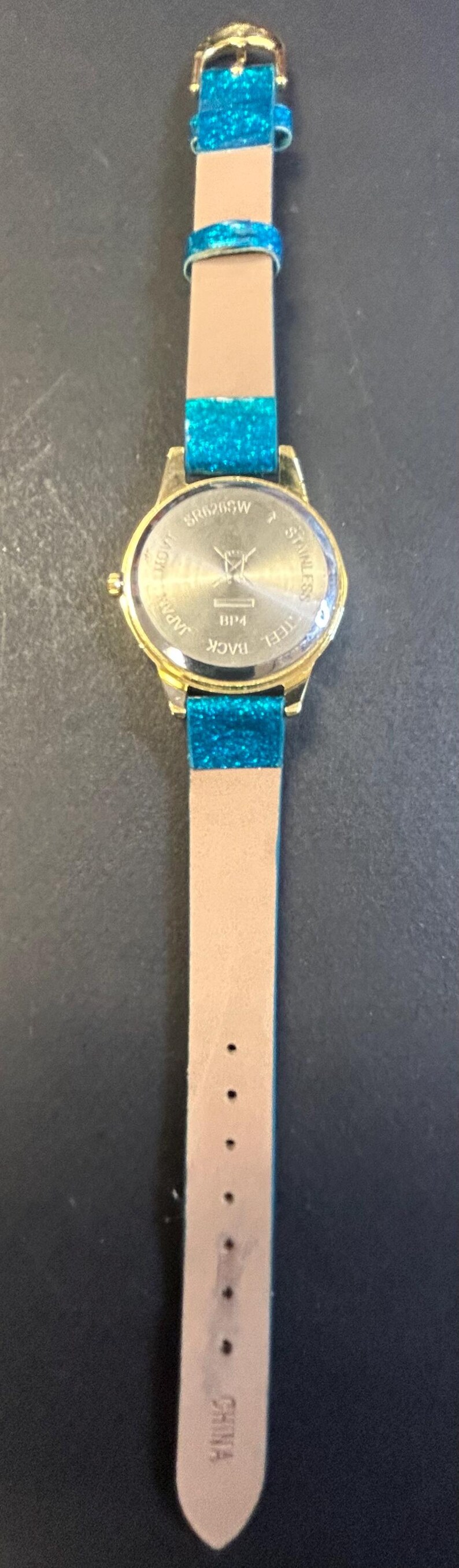 May include: Gold-toned wristwatch with a light brown band and teal glitter accents. The watch face is round with a gold bezel. The band has a buckle closure and is marked "CHINA".
