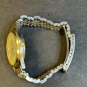 May include: A gold and silver two-tone watch with a round face and a metal band. The watch has a white dial with black markings and hands.