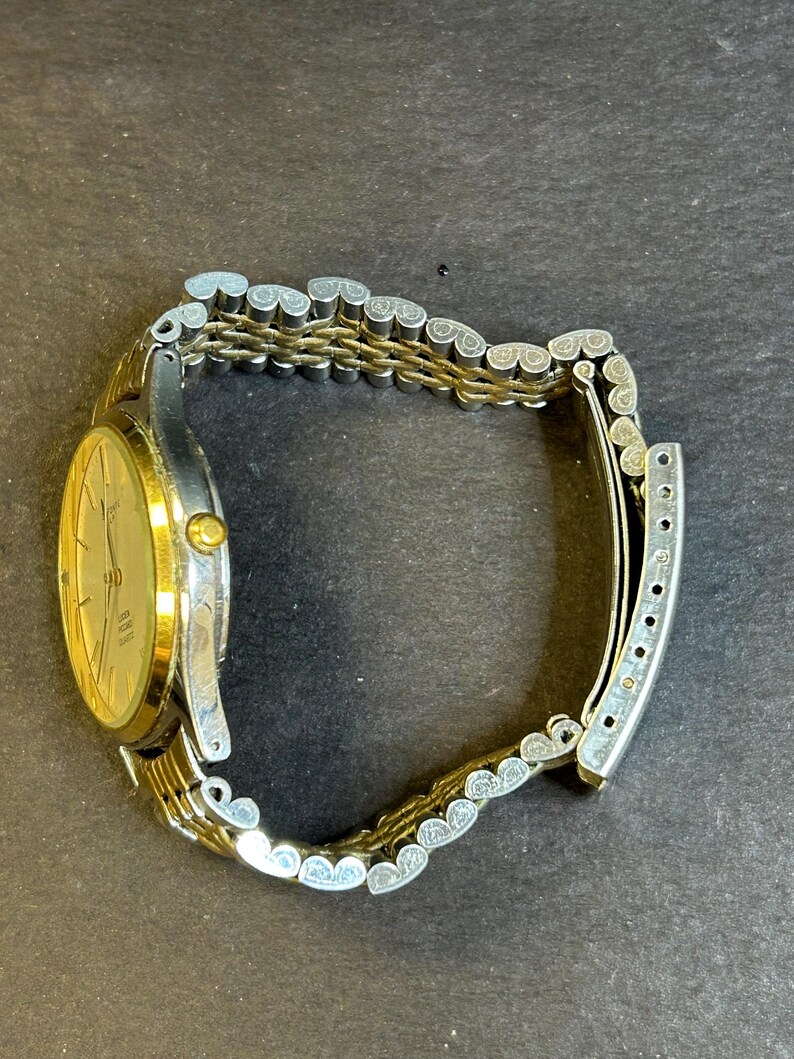 May include: A gold and silver two-tone watch with a round face and a metal band. The watch has a white dial with black markings and hands.