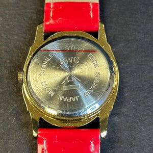 May include: Gold-tone watch with a red and white striped leather band. The back of the watch has the text "Stainless Steel Back SS W259SW Japan Mov't BWC".