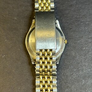 May include: A gold and silver two-tone watch with a metal band. The back of the watch has the text "BASEL" and "SWISS MADE" printed on it.