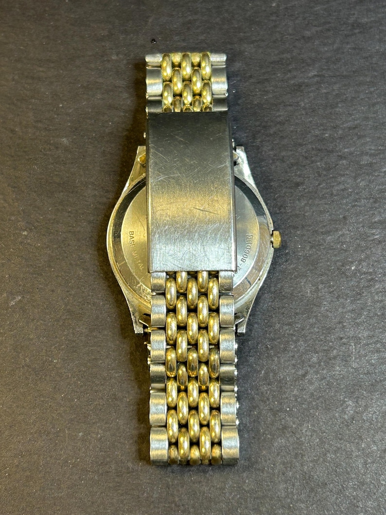 May include: A gold and silver two-tone watch with a metal band. The back of the watch has the text "BASEL" and "SWISS MADE" printed on it.