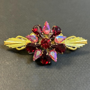 May include: A gold tone brooch with a cluster of red and pink rhinestones in a flower shape.