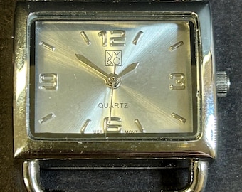 May include: A silver-toned watch with a square face and a silver metal band. The watch face has a white background with black markings and the words "NY & C" and "QUARTZ".