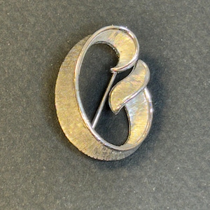 May include: Silver tone brooch in the shape of the letter "C".