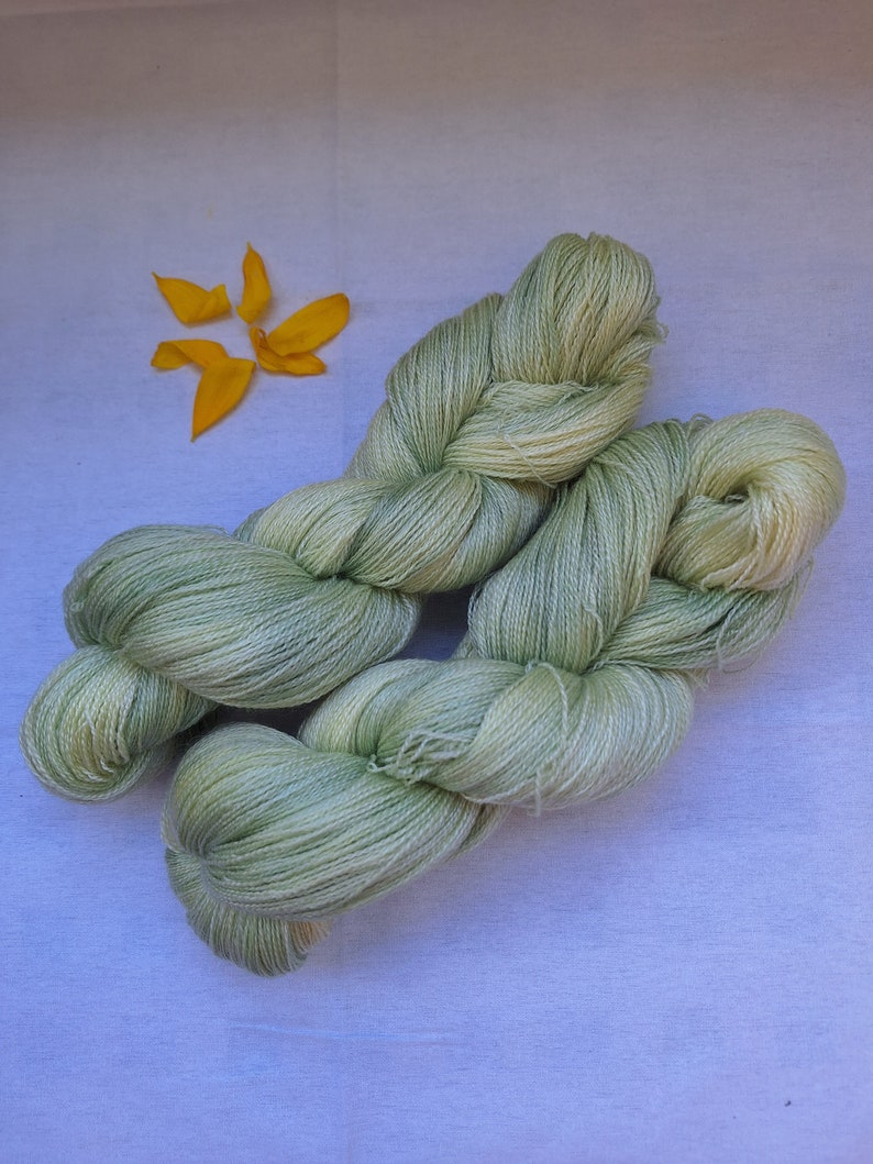 Pode incluir: Um novelo de fio verde claro, torcido e dobrado, sobre uma superf&iacute;cie branca.