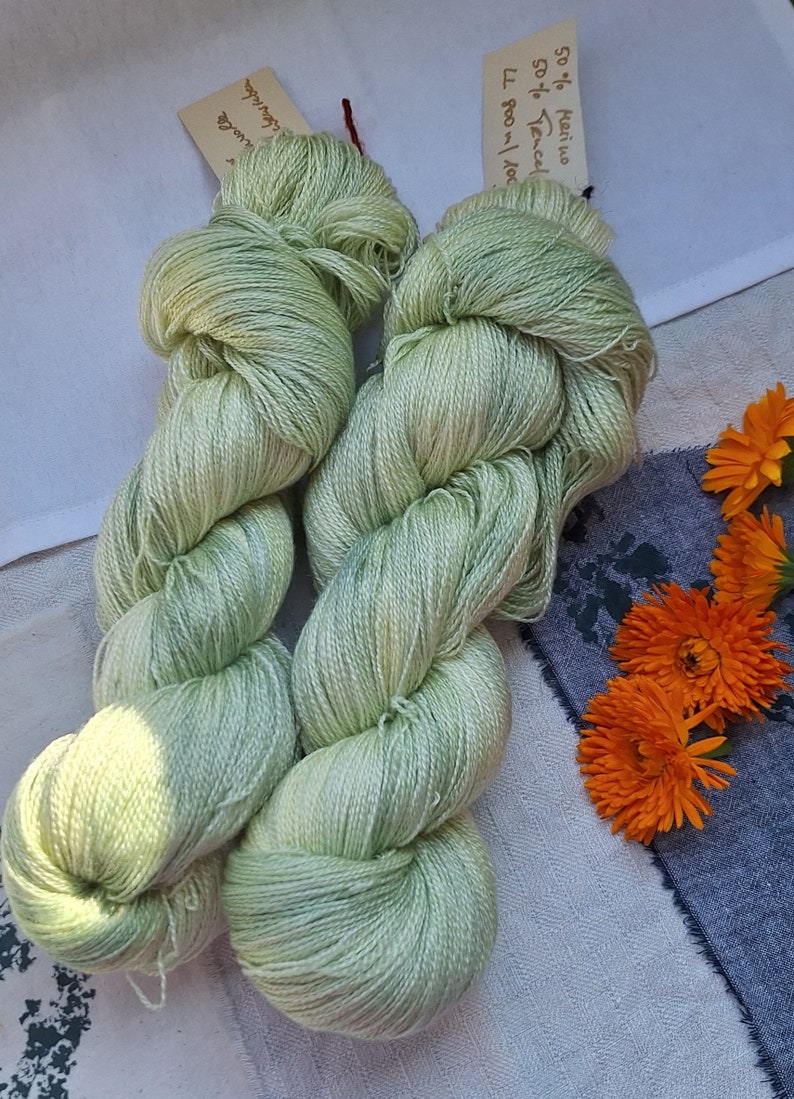 Pode incluir: Dois novelos de fio verde claro, 50% merino e 50% tencel, com um r&oacute;tulo que diz "50% merino 50% tencel 100g/3.5oz 77"