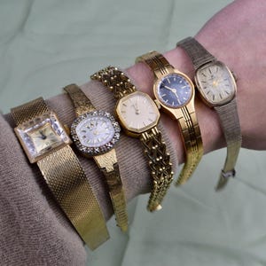 May include: A collection of five vintage gold-toned wristwatches, each with a unique design. The watches feature various band styles, including mesh, link, and textured bands. The watch faces showcase different shapes and colors, including a square, oval, and round face.