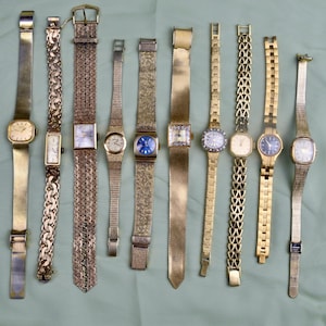 May include: A collection of vintage gold-toned wristwatches with various band styles, including mesh, chain, and textured designs. The watch faces are diverse, featuring square, rectangular, and round shapes, with some adorned with gemstones and intricate detailing.