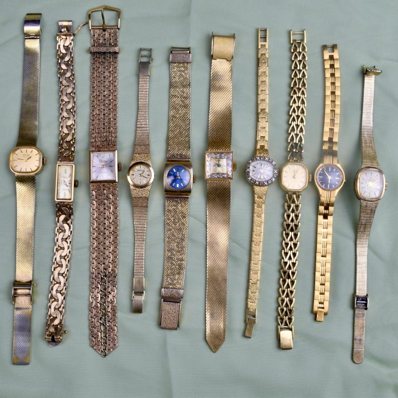 May include: A collection of vintage gold-toned wristwatches with various band styles, including mesh, chain, and textured designs. The watch faces are diverse, featuring square, rectangular, and round shapes, with some adorned with gemstones and intricate detailing.