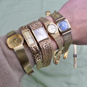 May include: A collection of vintage gold-toned wristwatches with various band styles, including mesh and linked designs. The watch faces are in different shapes, with some featuring Roman numerals and a blue face.