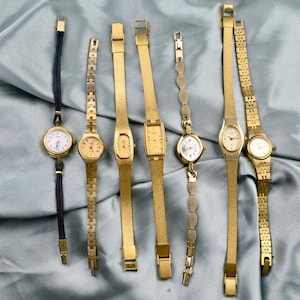 May include: A selection of vintage gold-coloured wristwatches with diverse strap designs. The watches have round, oval, and rectangular faces with white dials and black numerals. Some have mesh straps, others link straps, and one has a black cord strap.