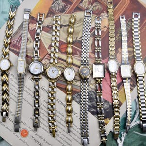 May include: A collection of ten wristwatches with metal link bands in various silver and gold-tone finishes. The watches feature diverse case shapes including round, oval, and rectangular, with white, cream, and dark dials and analog displays.