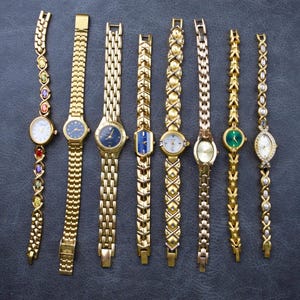 Pode incluir: Uma coleção de oito relógios de pulso dourados com vários designs de mostrador e estilos de pulseira. Alguns relógios apresentam pedras preciosas coloridas, enquanto outros têm mostradores azuis, brancos ou verdes. As pulseiras incluem elos, correntes e padrões decorativos.