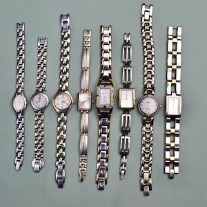 May include: Nine wristwatches with silver and gold-tone metal straps. The watch faces are oval, square, and round, with white or gold dials. Some watches have decorative features. The watches are displayed on a light green surface.