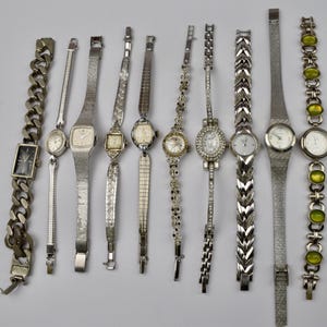 Könnte beinhalten: Sammlung von Vintage-Uhren in Silberoptik mit verschiedenen Armbandstilen. Merkmale sind rechteckige, quadratische und runde Zifferblätter. Einige Armbänder sind kettenartig, andere filigran und einige mit Edelsteinen verziert. Eine Vielzahl klassischer Zeitmesser.