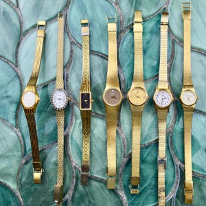 Può includere: Una collezione di orologi da polso dorati con vari stili di cinturino e design del quadrante. Gli orologi presentano quadranti rotondi, ovali e rettangolari, alcuni con dettagli di diamanti. I cinturini includono modelli a maglia, a maglie e pieni.
