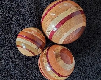 May include: Three wooden spheres of varying sizes, each crafted with a striped design. The spheres feature alternating bands of light and dark wood, with accents of red. The largest sphere is approximately 6 inches in diameter, the smallest is about 3 inches.
