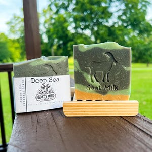 May include: Two bars of Deep Sea goat milk soap with a green and orange marbled design. One bar features a goat silhouette and the text Goat Milk, while the other has a paper label reading Cedar Hill Handmade Soaps, Deep Sea, and 4oz.