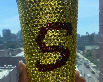 Può includere: Un bicchiere giallo ricoperto di strass con una lettera "S" in strass rosso sul davanti.