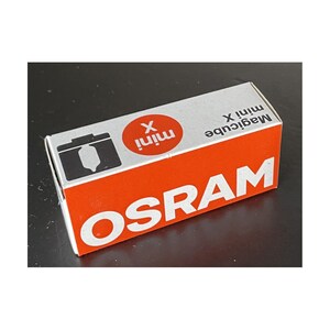 Peut inclure: Boîte rectangulaire orange et blanche avec le nom de la marque « OSRAM » en grandes lettres blanches. Le dessus de la boîte affiche « Magicube mini X » et un dessin de caméra. Produit photographique.