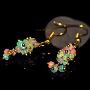 May include: A pair of gold-toned earrings featuring clusters of iridescent opal beads. The opal beads display a range of colors, including pink, green, and blue, and are connected by delicate gold wire. The earrings have a hook closure.
