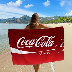 May include: A red beach towel with a white Coca-Cola logo and the words "cherry" printed on it.