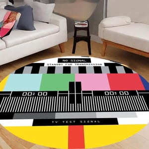 May include: A round rug featuring a colorful TV test pattern design. The rug has a yellow border, with sections of red, pink, green, and blue. The text "NO SIGNAL STANDBY FOR TRANSMISSION" is displayed at the top.