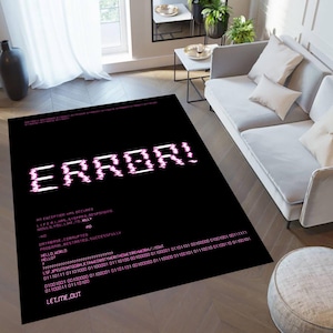 Puede incluir: Alfombra rectangular negra con la palabra "ERROR!" en fuente pixelada rosa. La alfombra tiene texto rosa adicional, incluido código binario y frases como "LIFE HAS STOPPED RESPONDING" y "LET ME OUT".